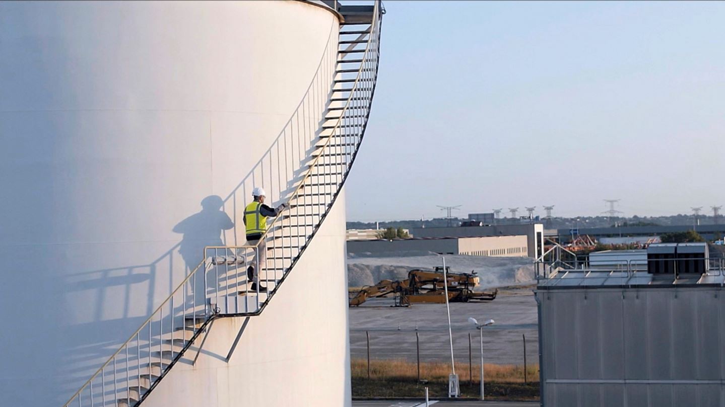 man in safety gear climbing stairs around large industrial gas storage tank