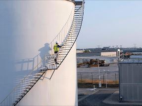 man in safety gear climbing stairs around large industrial gas storage tank